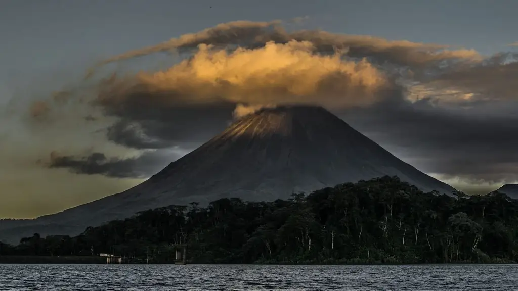 Stunning view of Arenal Volcano with glowing clouds at dusk in Costa Rica, surrounded by lush forest and tranquil waters