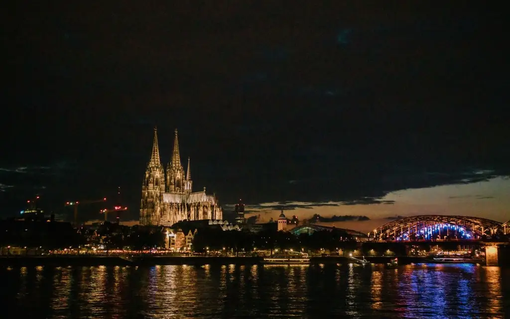 View of Cologne Cathedral and Hohenzollern Bridge illuminated at night, reflecting in the Rhine River