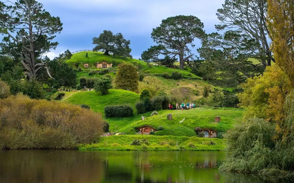 Lush green landscape of Hobbiton with iconic hobbit holes and serene lake reflecting the vibrant scenery
