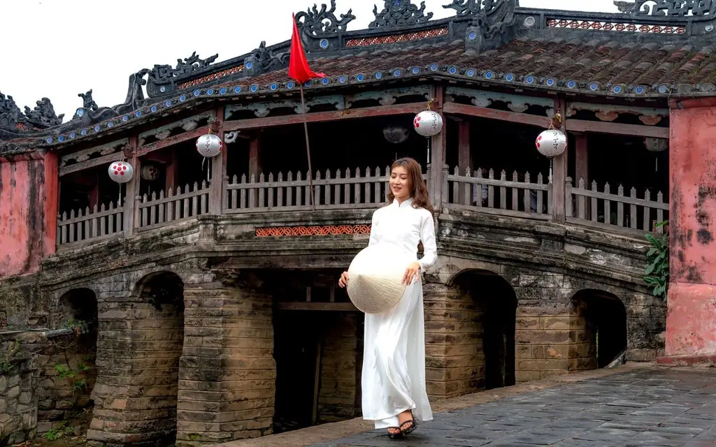 A woman in traditional Vietnamese attire stands by the Hoi An Japanese Bridge