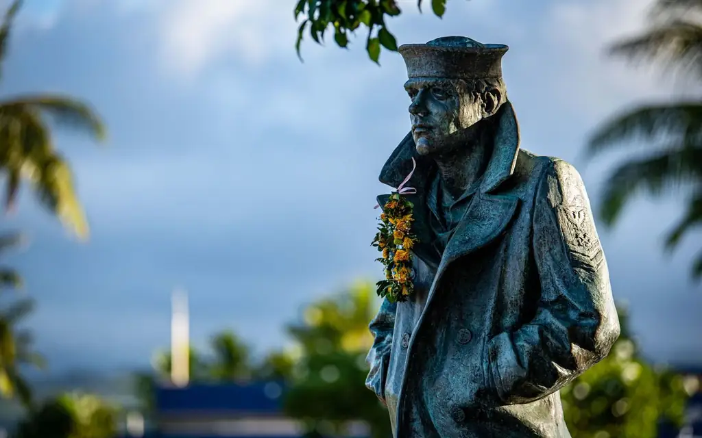 Bronze statue of a sailor at Pearl Harbor memorial adorned with a floral lei
