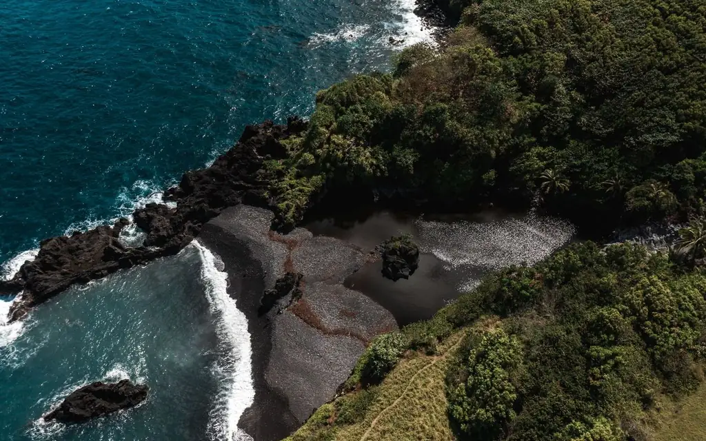 A stunning aerial shot of a black sand beach surrounded by lush greenery in Hana, Hawaii