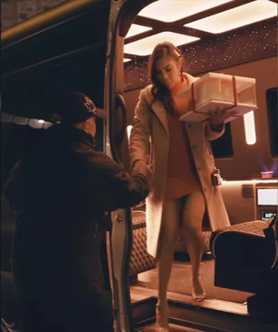 A chauffeur helps a passenger carrying a gift box step down from a Jet Sprinter at night