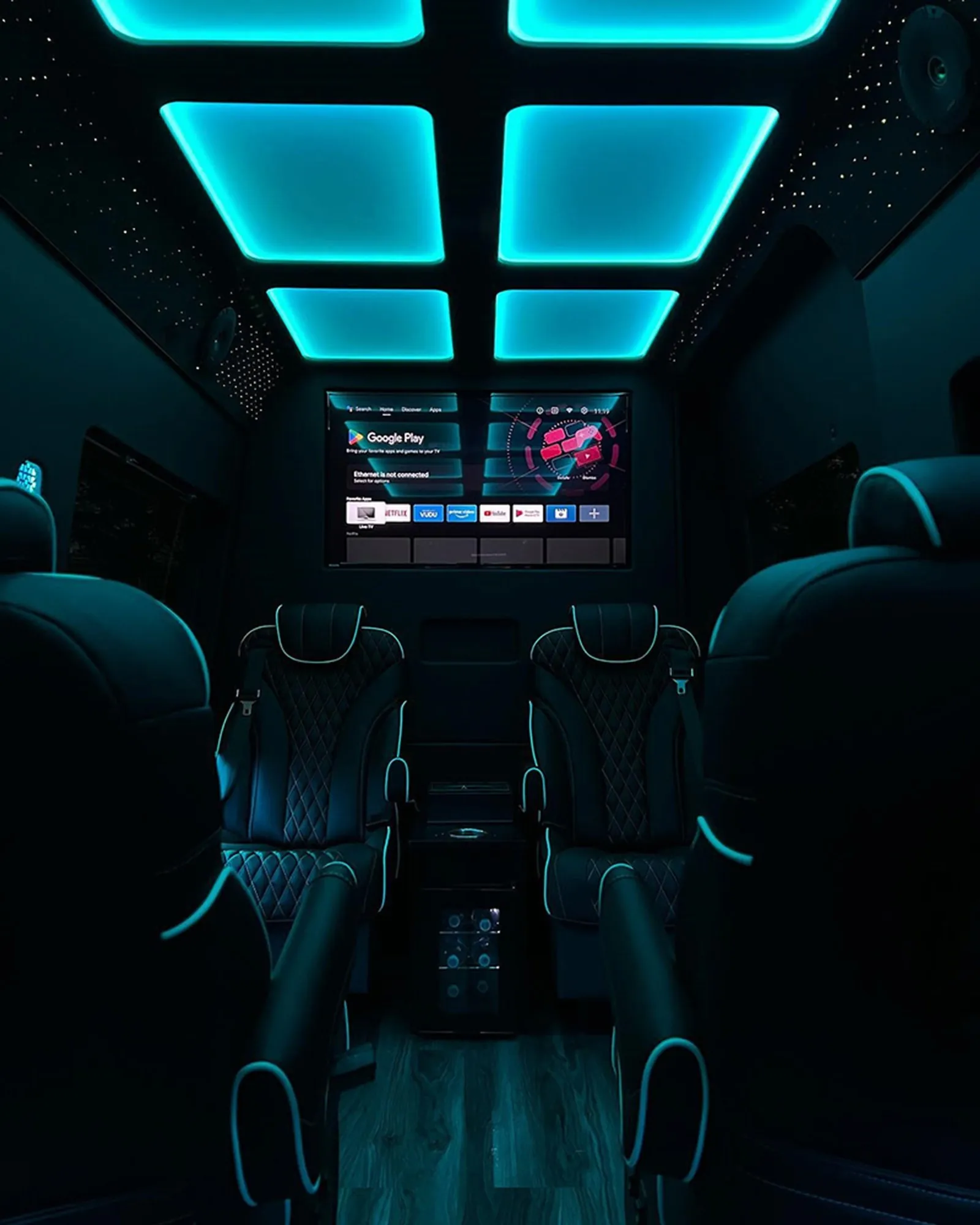 Jet Sprinter cabin in teal mood lighting with captain's chairs facing a wall-mounted streaming screen