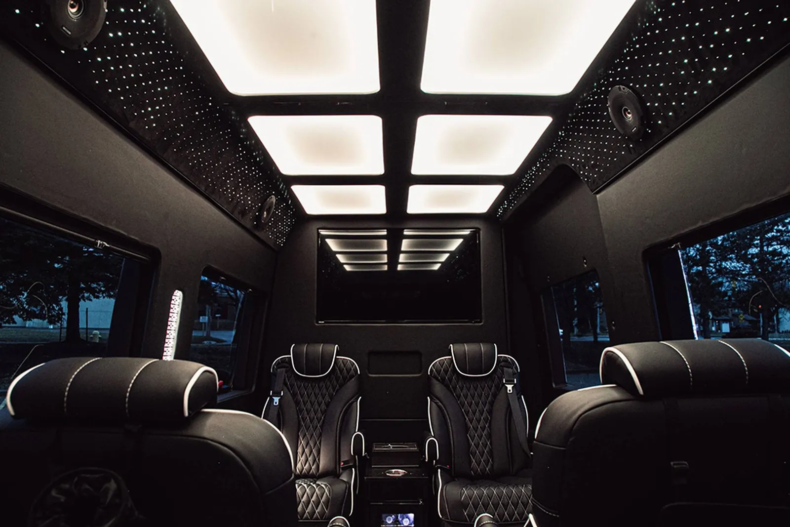 Jet Sprinter cabin with white ceiling light panels, a starlight headliner, quilted leather captain's chairs and a screen
