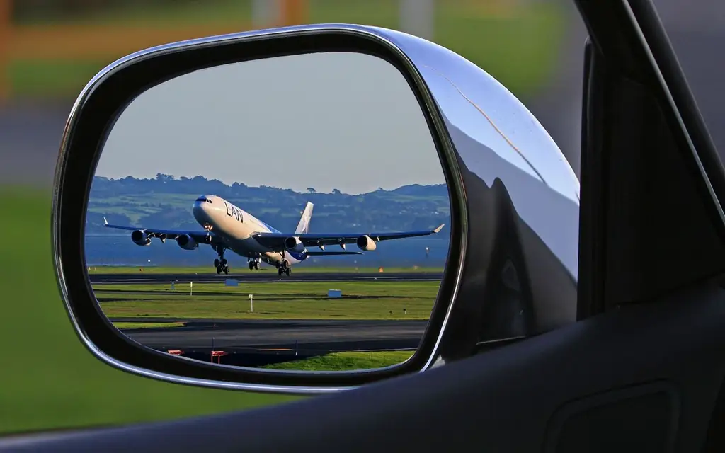 A jet airplane taking off is reflected in a car's side mirror, capturing a unique aviation perspective