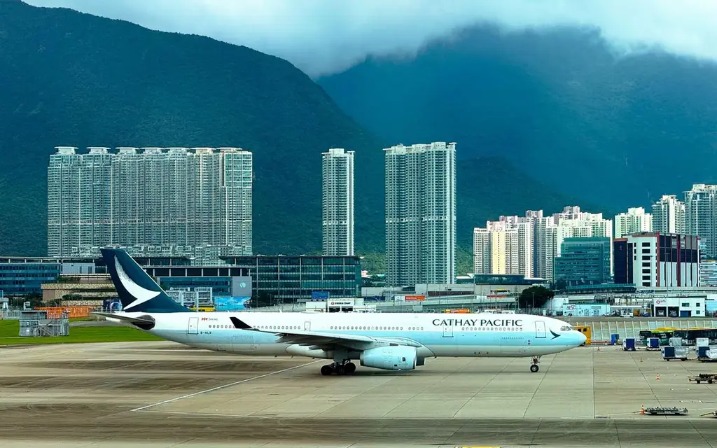 Cathay Pacific airplane taxiing on runway with Hong Kong skyline and mountains in the background