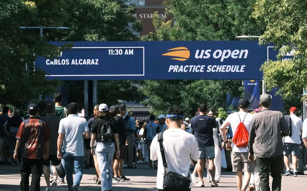 People gather at the US Open practice schedule board under clear skies