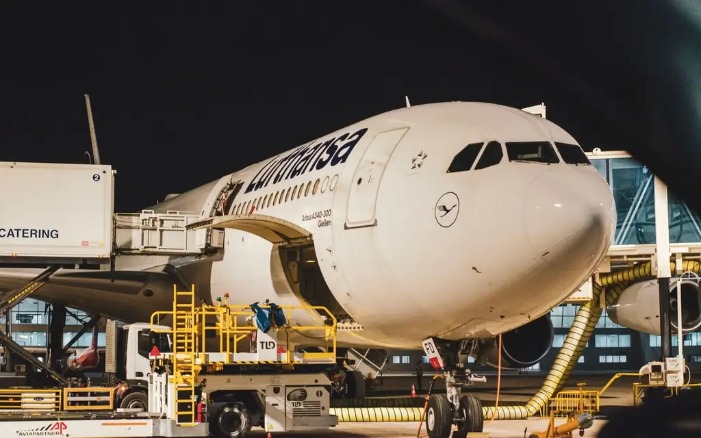 Night view of a Lufthansa airplane docked at an airport terminal with ground services working