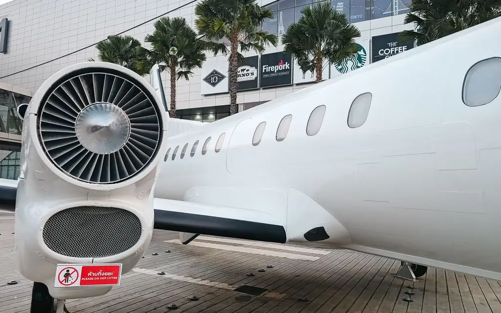 Private jet parked at a modern airport terminal with palm trees and shopping signs visible