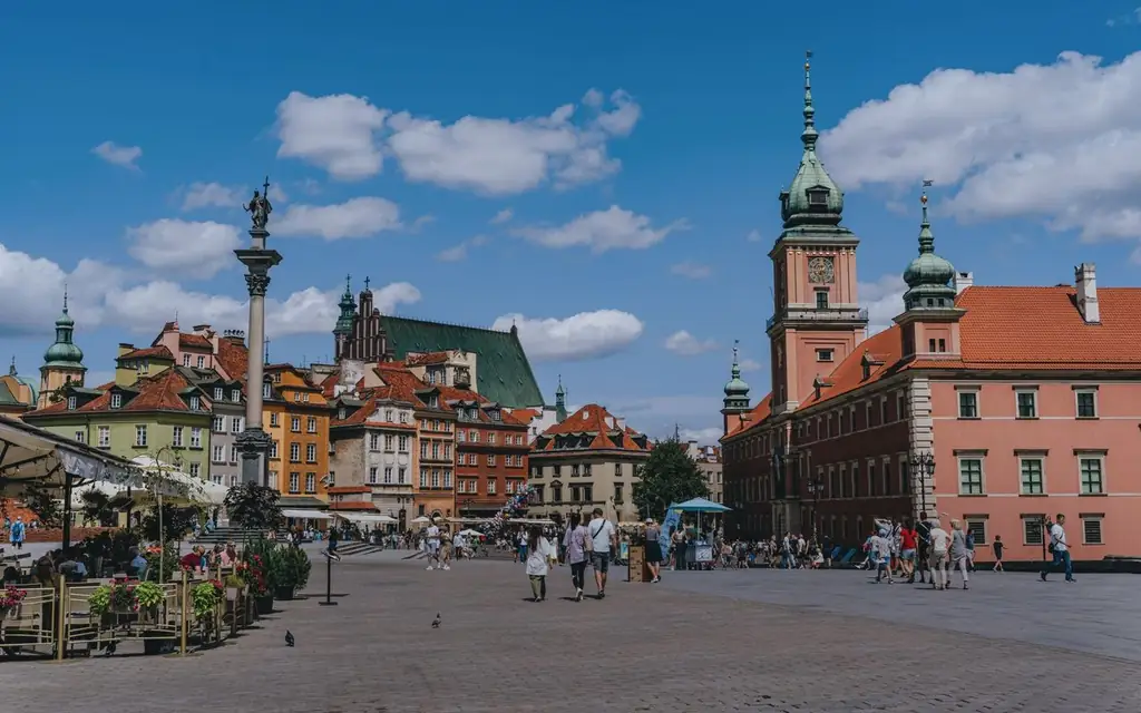 Vibrant scene of Warsaw's Old Town Square with tourists and iconic landmarks under a blue sky